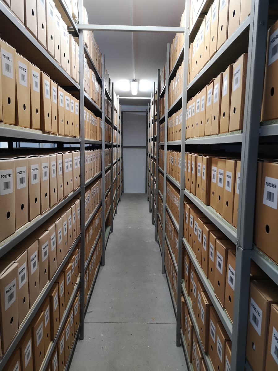 Regały archiwalne z opisanymi pudłami w magazynie archiwum